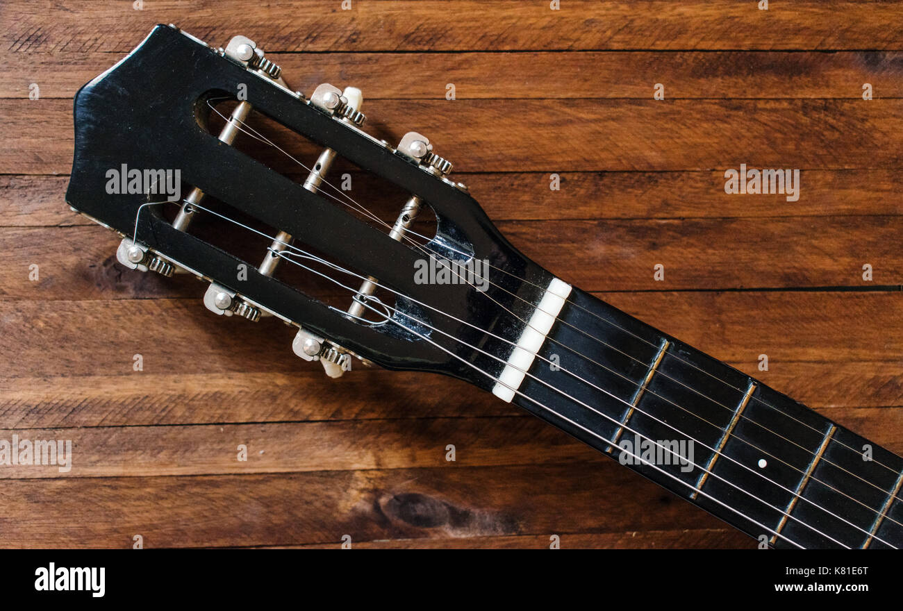 Guitare acoustique noire, tête de l'écrou, chevilles et cordes, sur une vieille table en bois brun, fond avec beaucoup de texture background et lignes Banque D'Images