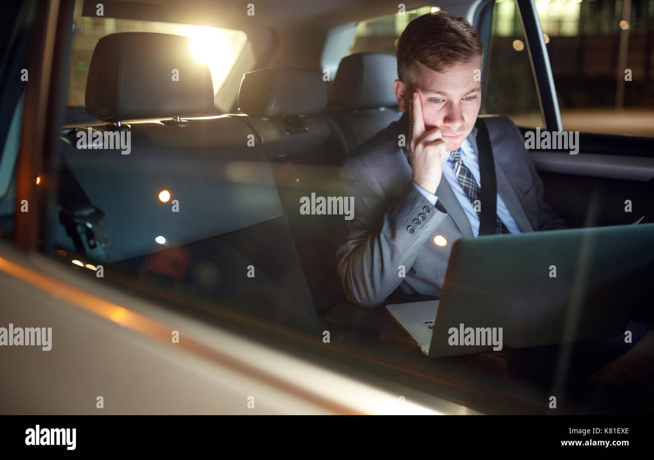 Serious businessman en voiture en heures supplémentaires de travail sur son ordinateur portable Banque D'Images