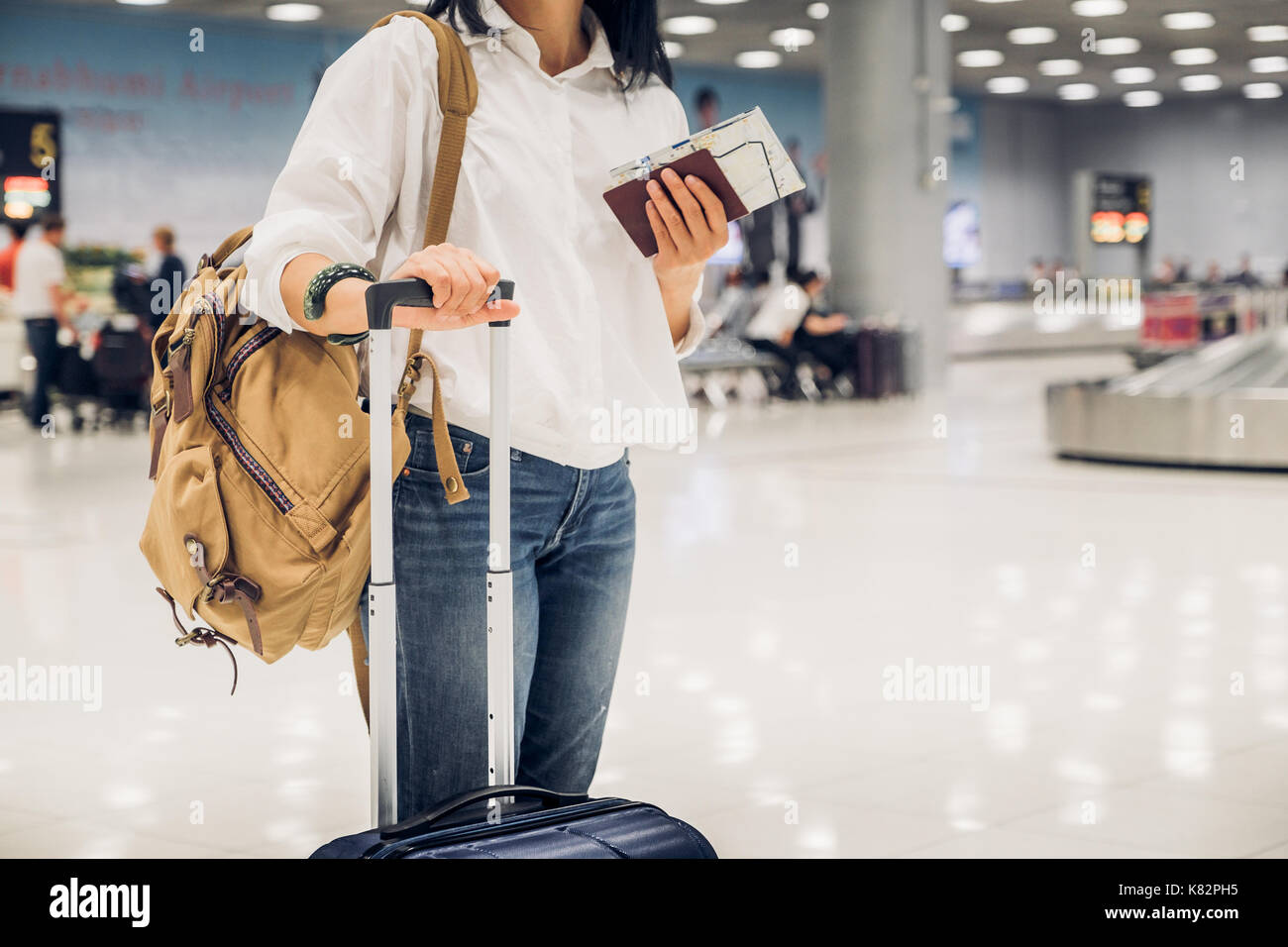 Woman backpacker holding passeport et carte avec valise debout à l'arrivée dans les bagages à l'aéroport,meilleur concept. Banque D'Images