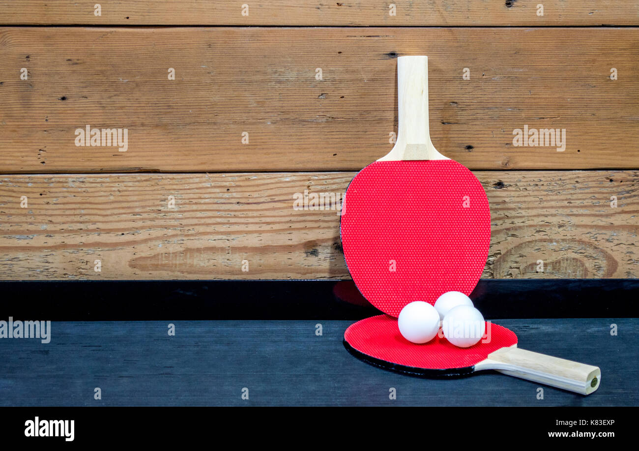 Rouge 2 raquettes et 3 balles de ping-pong blanches sur un plateau noir contre un mur en bois Banque D'Images