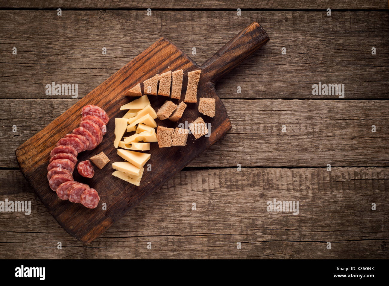Planche à découper, de salami, de fromage et de pain sur fond de bois foncé Banque D'Images