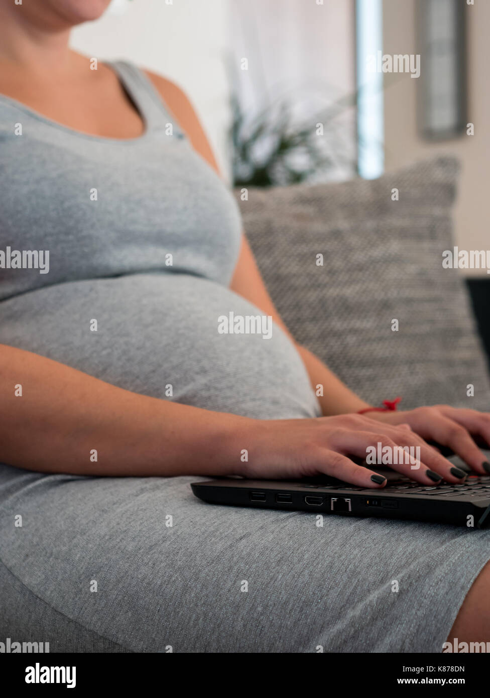 Pregnant caucasian woman sitting on couch à la maison et travailler sur l'ordinateur portable en ligne Banque D'Images