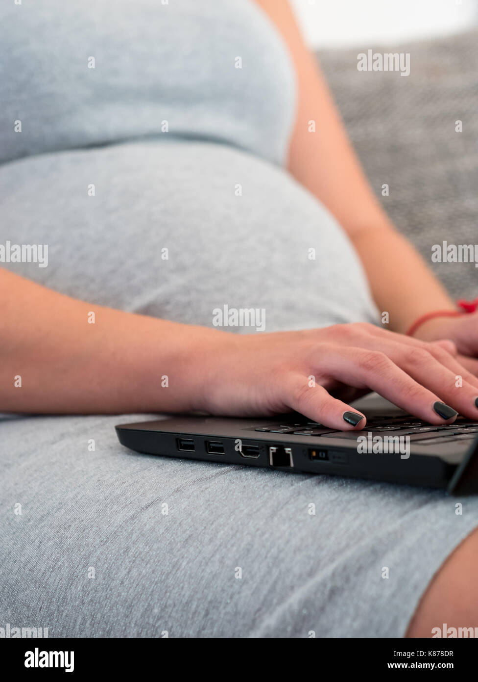 Pregnant woman sitting on couch et de travail sur l'ordinateur portable en ligne close up Banque D'Images