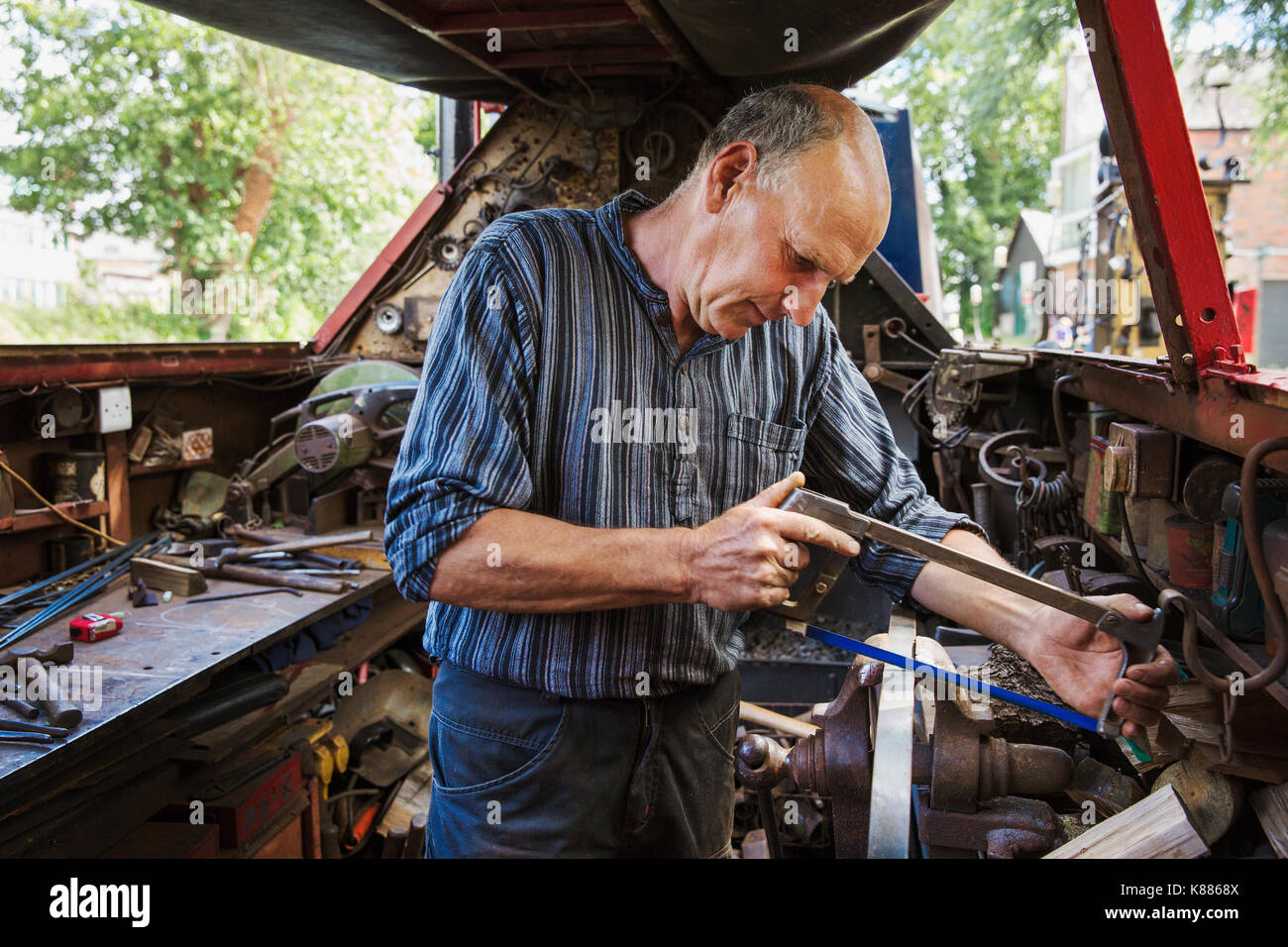 Dans son atelier de forgeron sur une barge de travail, à un établi, à l'aide d'une scie à métaux. Banque D'Images