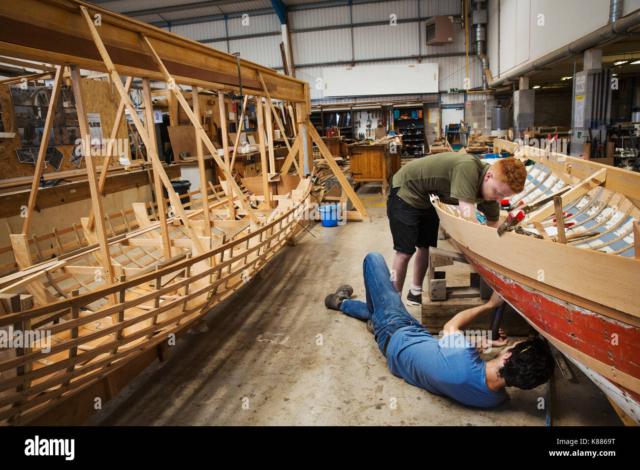 Deux hommes dans un bateau-atelier du constructeur, travaillant ensemble sur un bateau en bois coque. Banque D'Images