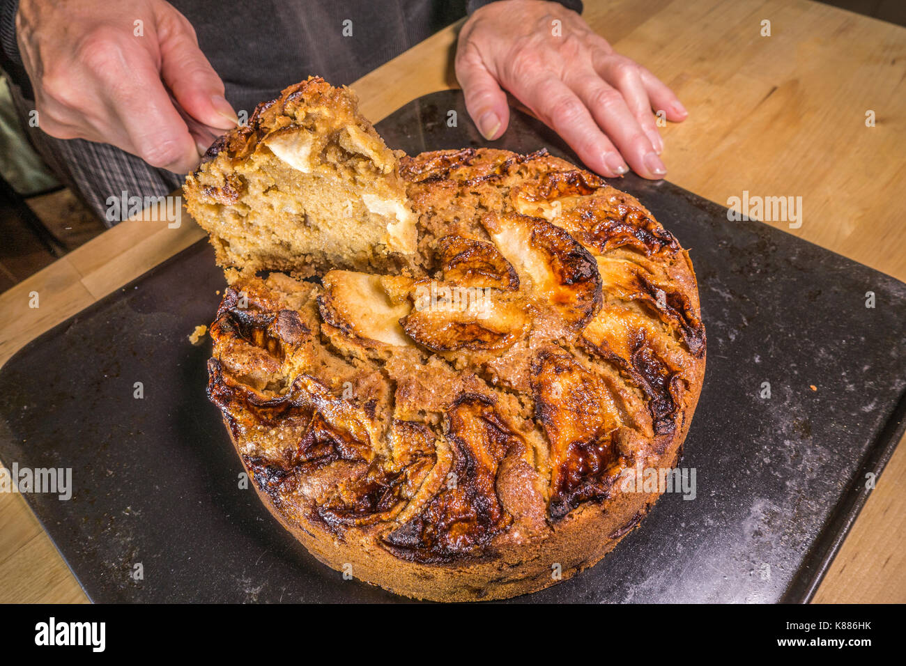 A woman's hands holding a triangular tranche de gâteau aux pommes épicées, de refroidissement sur une plaque de cuisson dans la cuisine, de l'étuve. Angleterre, Royaume-Uni. Banque D'Images
