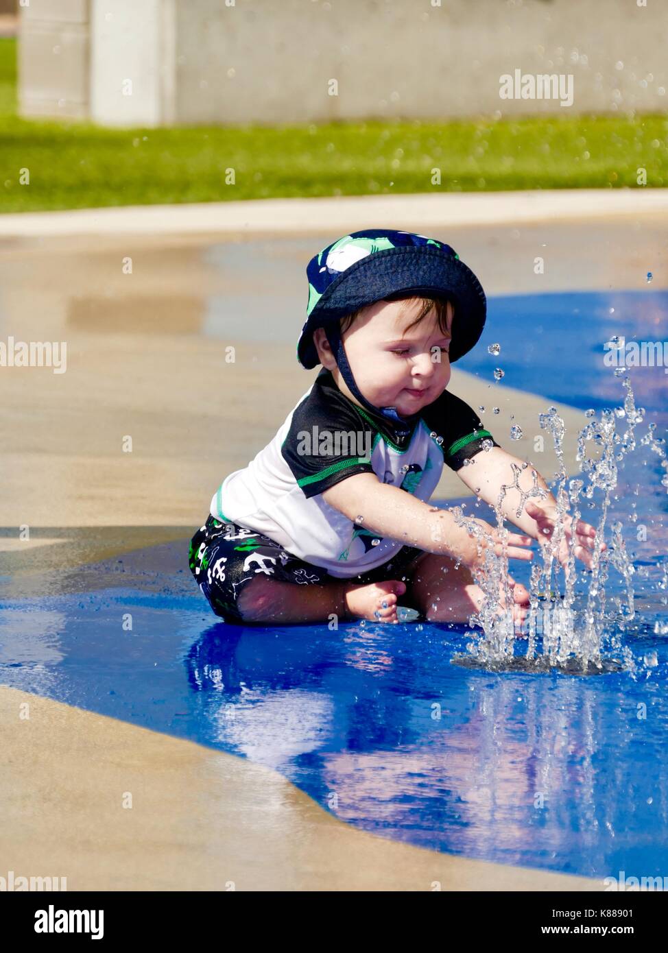 Bébé garçon, assis, vêtu de mignon maillot de bain, t-shirt et un chapeau,  jouer avec l'eau de pulvérisation au parc. En Floride, aux États-Unis Photo  Stock - Alamy