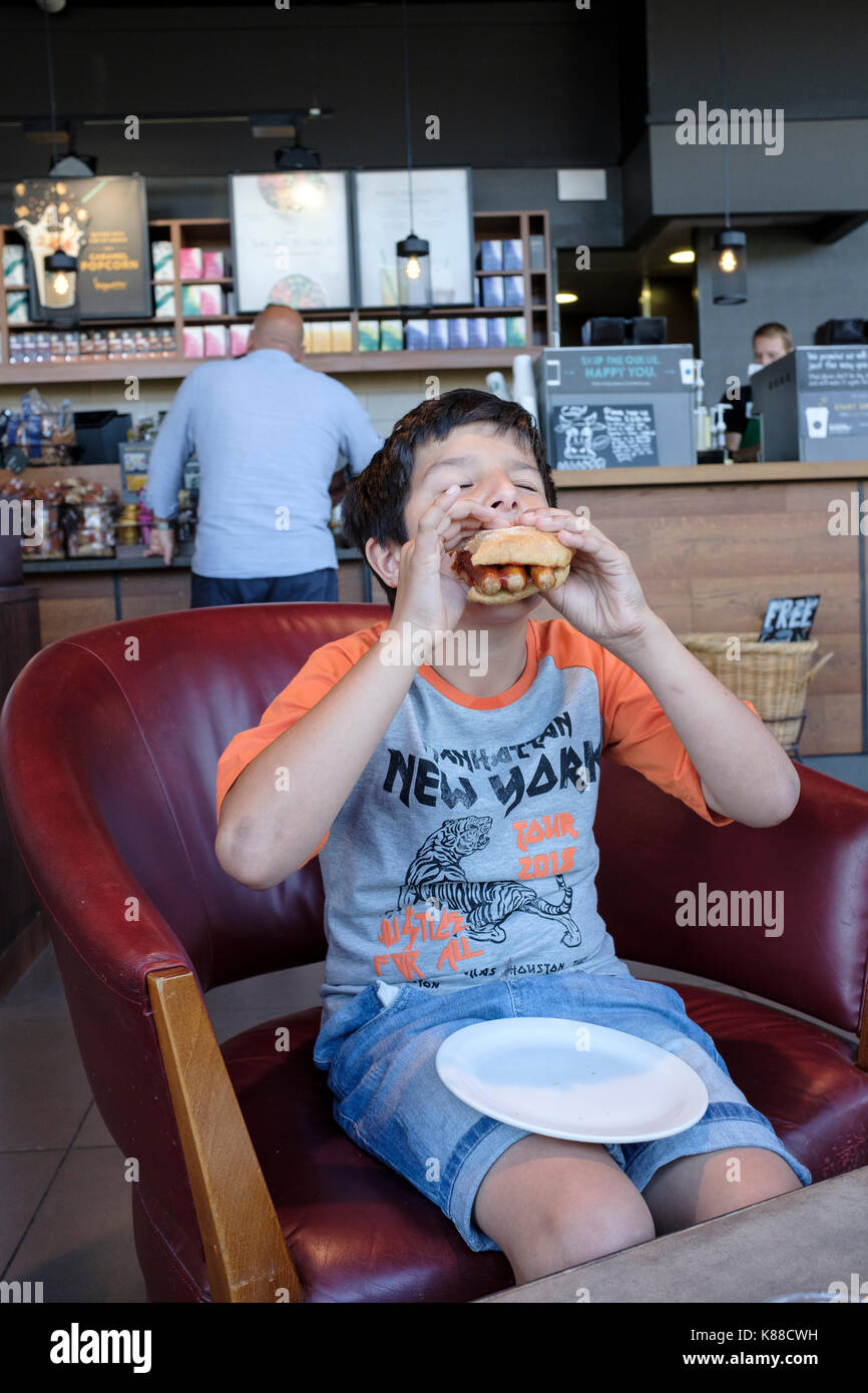 Garçon mange un sandwich au saucisson cafe,London,UK Banque D'Images