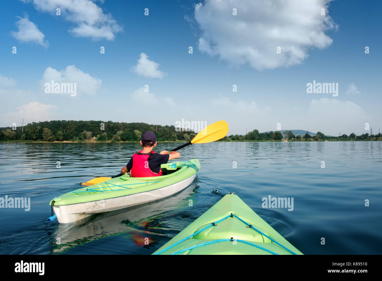 Garçon en veste verte sur kayak. journée ensoleillée sur le lac merveilleux. L'heure d'été Banque D'Images