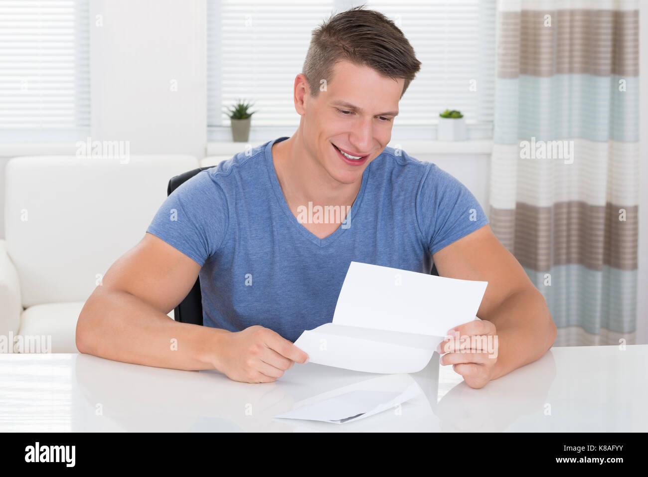 Heureux jeune homme lire une lettre envoyée au bureau Banque D'Images