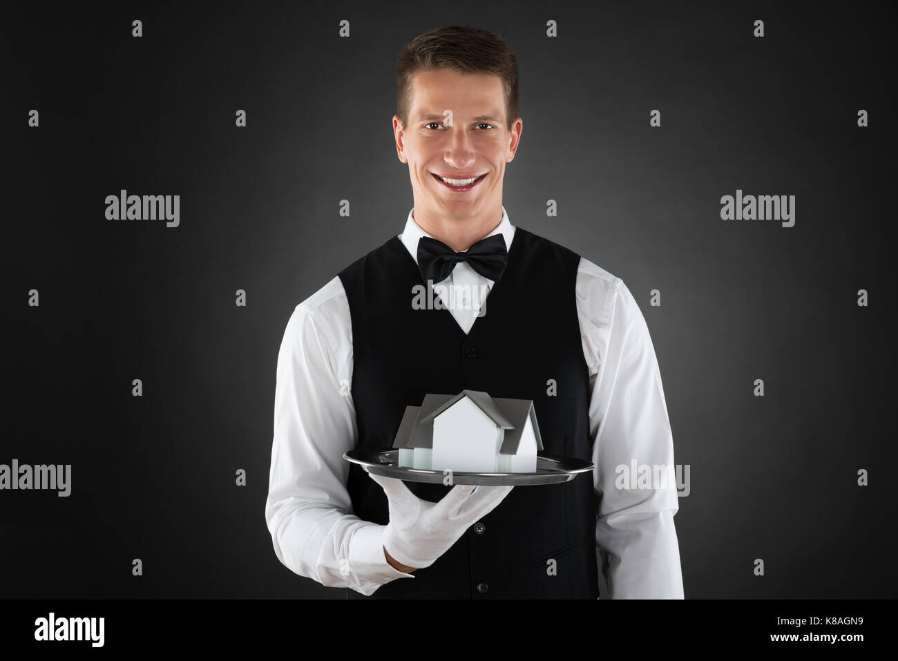 Young happy waiter holding tray with miniature house Banque D'Images