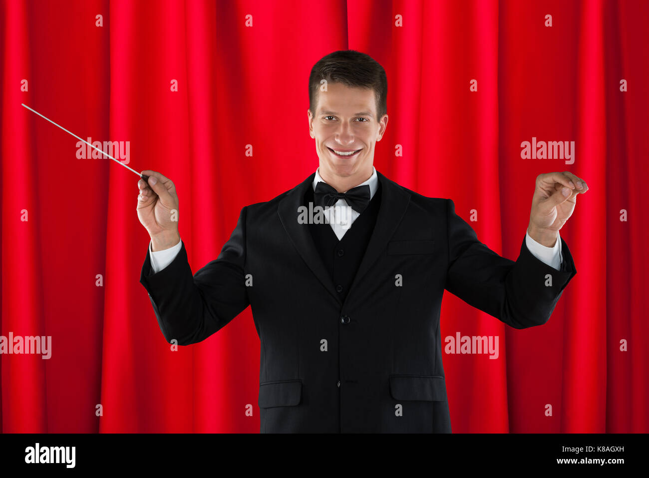 Homme d'orchestre holding baton sur rideau rouge Banque D'Images