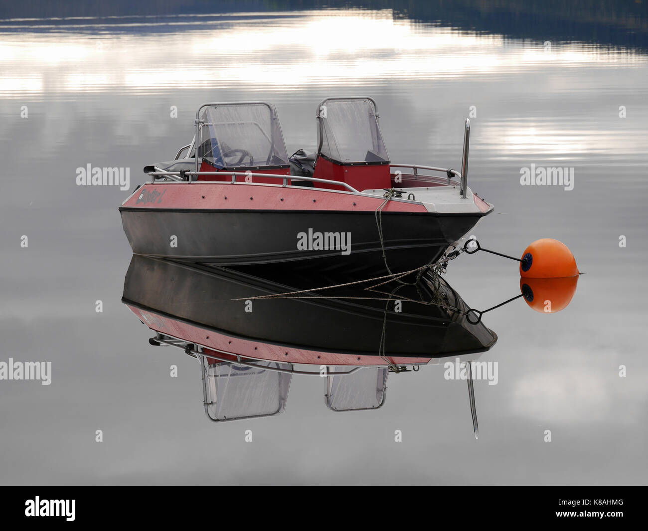 Le bateau en aluminium Buster se reflète dans le lac calme Åresjön, Åre, Jämtland, Suède. Le garçon Orange sécurise le bateau. Banque D'Images