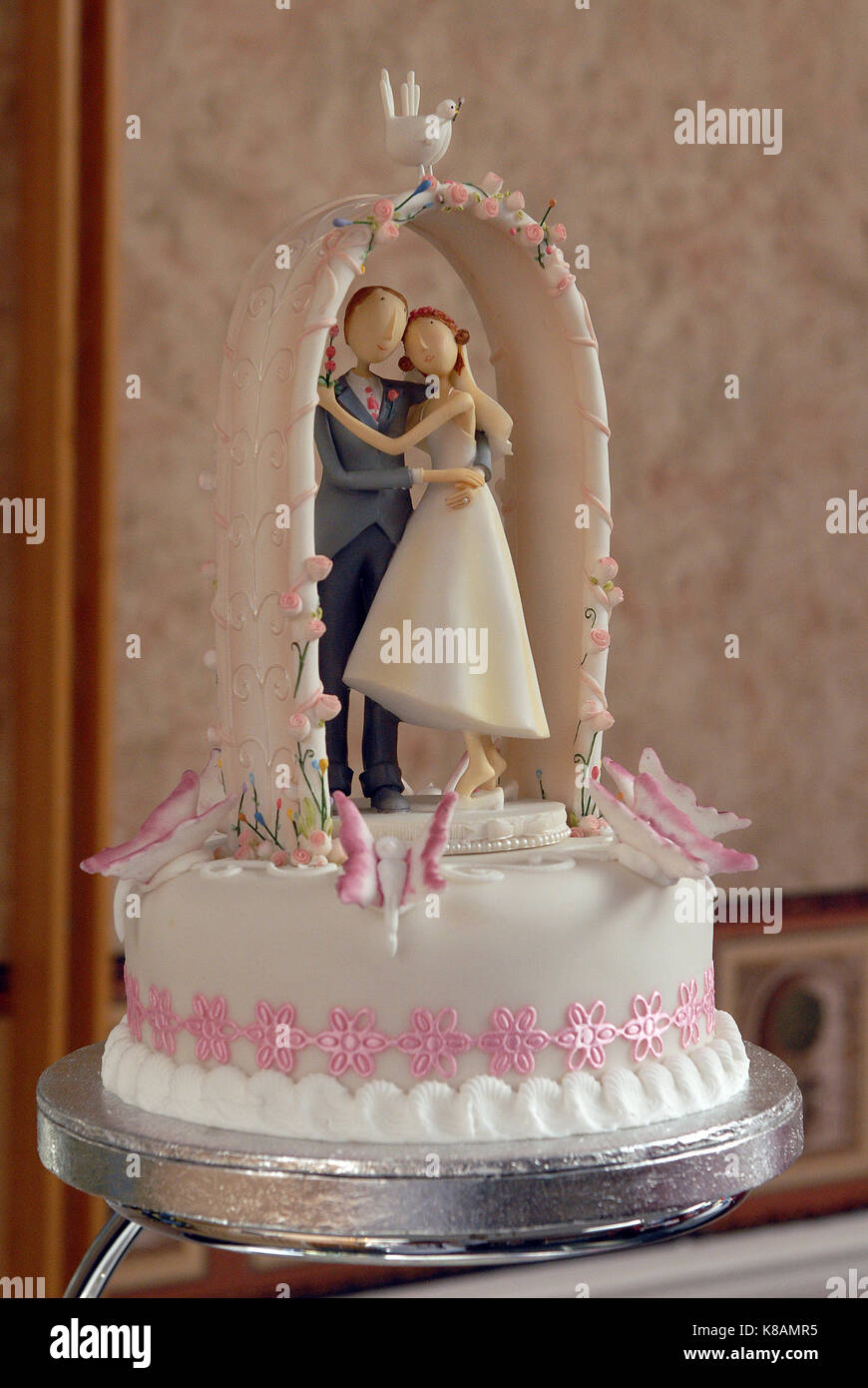 L Etage Superieur D Un Gateau De Mariage Avec Un Modele D Une Femme Et Un Homme Debout Sur Le Gateau Sous Une Arcade Rose Et Blanc Et Cerise Sur Le Gateau Photo Stock
