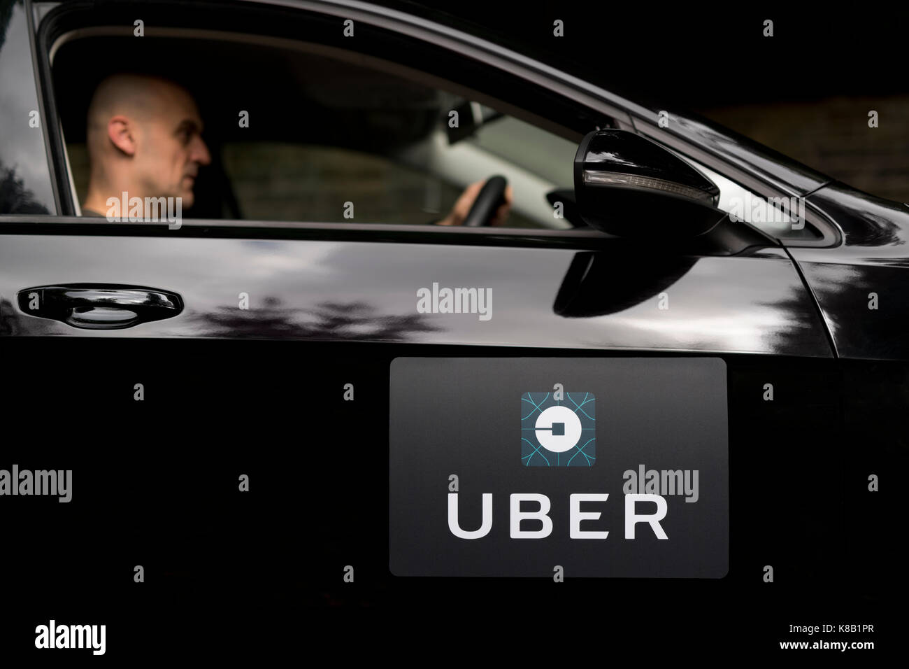 Une Volkswagen noire avec le logo Uber est utilisé comme un taxi et montre également un pilote dans une rue de banlieue verdoyante au Royaume-Uni (usage éditorial uniquement). Banque D'Images