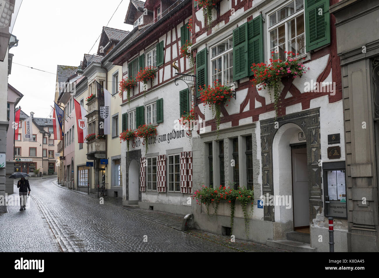 Homme marchant dans une rue avec des maisons à colombages avec des géraniums sur les appuis de fenêtre, Bregenz, Autriche Banque D'Images