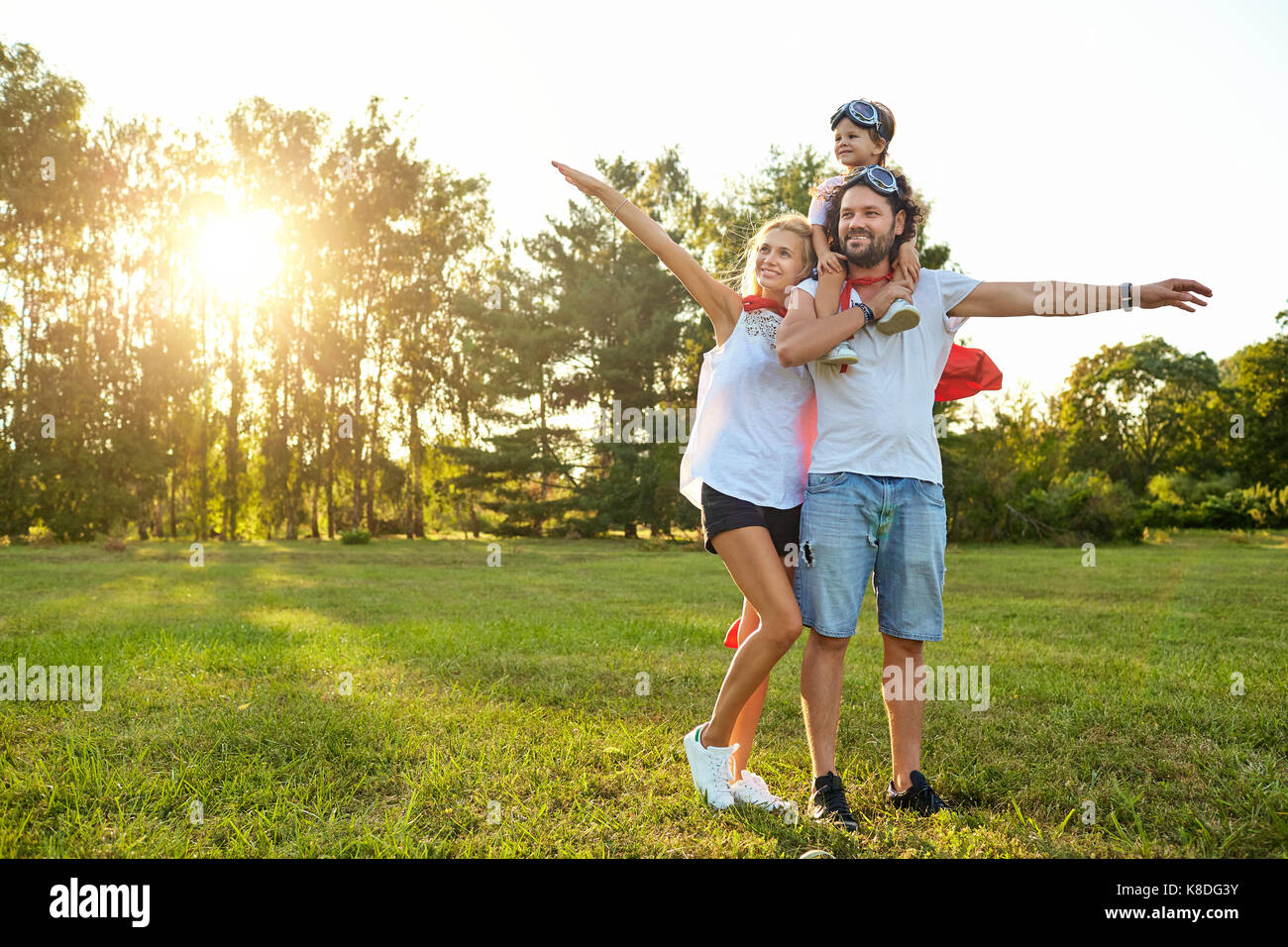 Famille heureuse en costume de super-héros dans le parc au coucher du soleil Banque D'Images