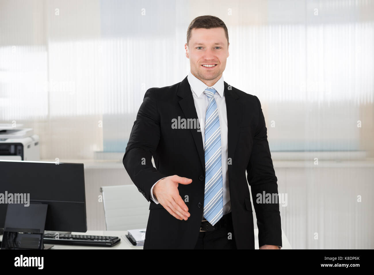 Portrait of happy businessman offrant tout en se tenant à l'ordinateur poignée desk in office Banque D'Images