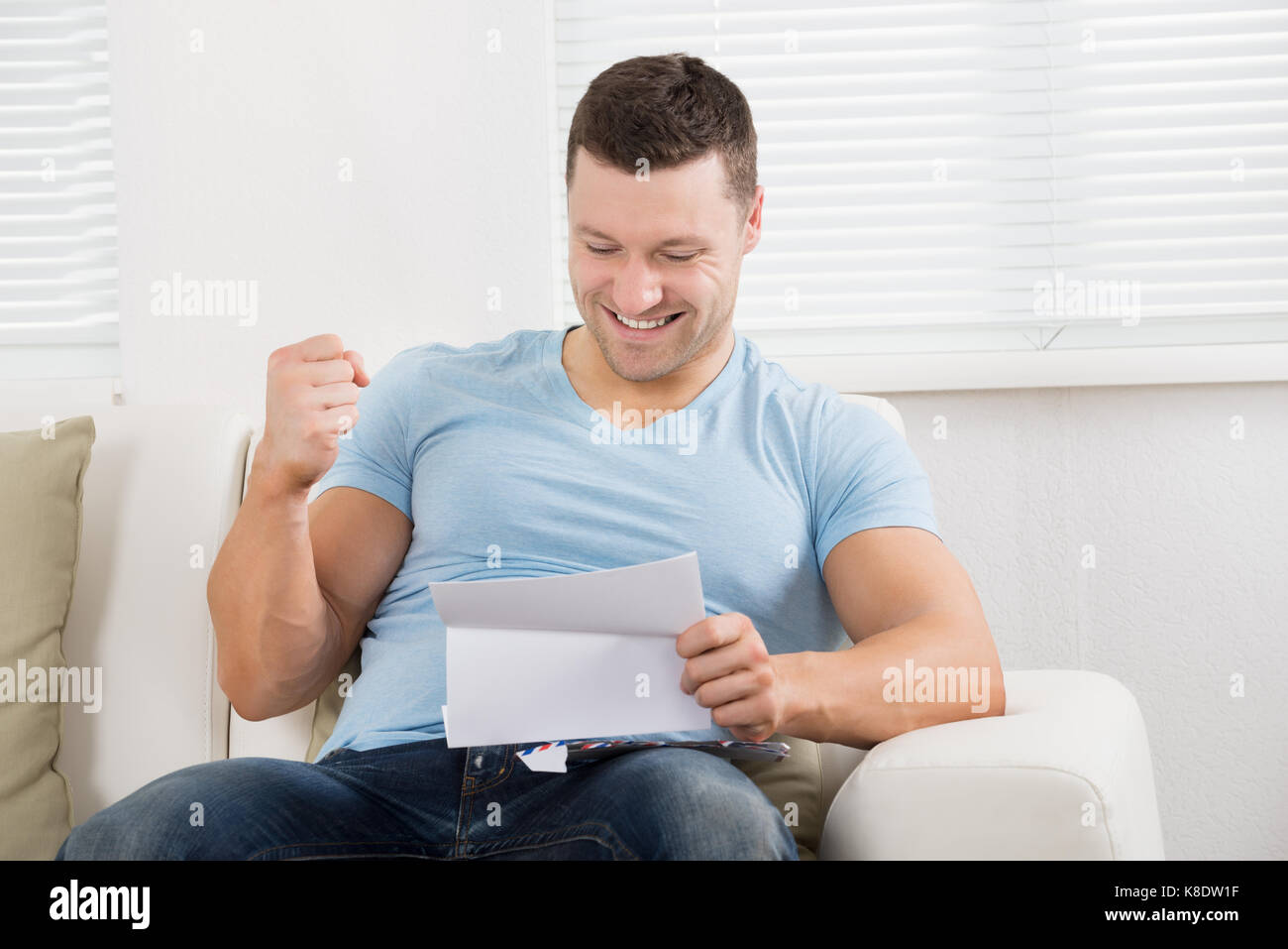 Happy Mid adult businessman clenching fist lors de la lecture de lettre sur canapé à la maison Banque D'Images