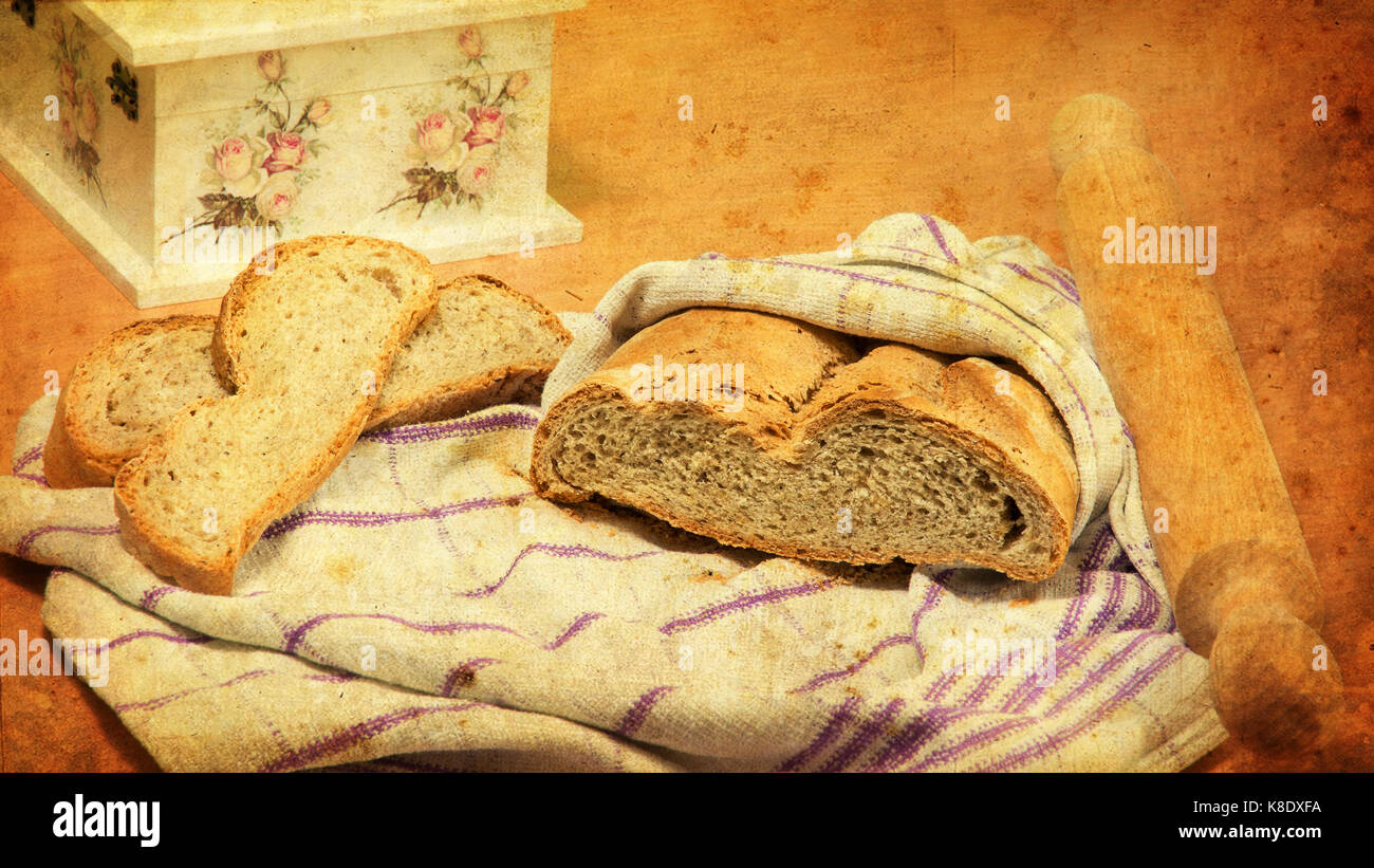 Du pain enveloppée dans un torchon, deux tranches de pain à côté de lui, et d'un rouleau à pâtisserie. superbe boîte de découpage est partiellement visible. look vintage. Banque D'Images