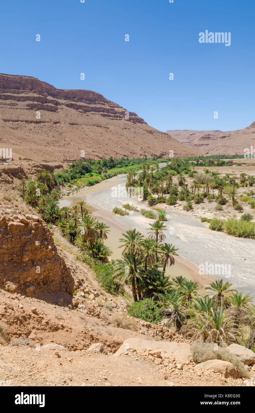 Lit de rivière à sec bordée de palmiers avec orange rouge montagne au Maroc, l'Afrique du Nord. Banque D'Images