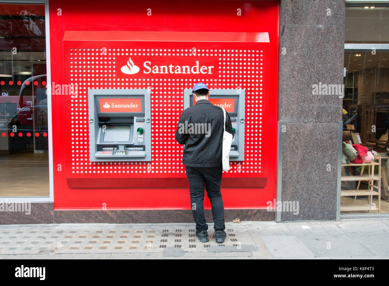 Un jeune homme debout devant un guichet automatique sur Tottenham Court Road, Londres, UK Banque D'Images