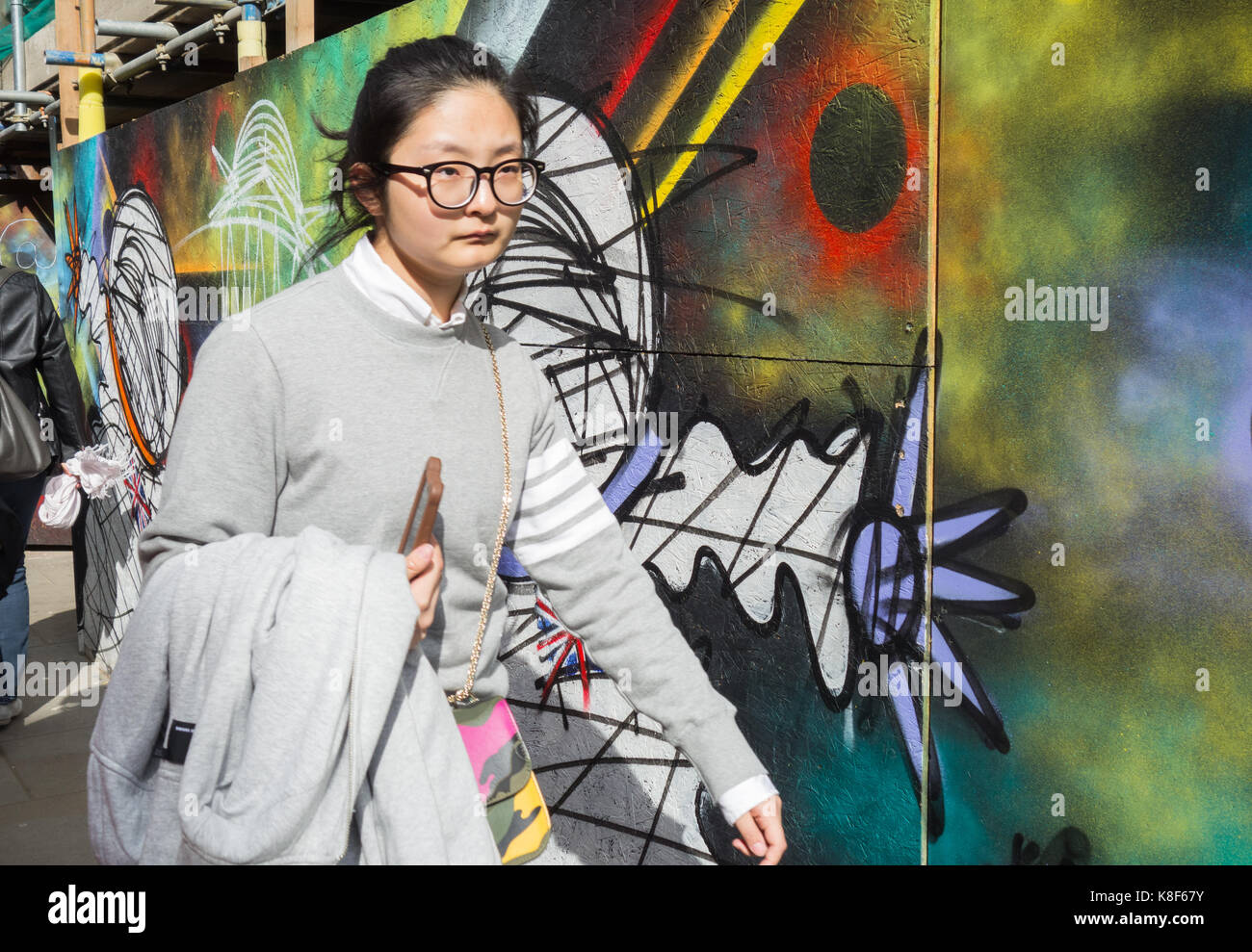 Une jeune femme marche devant un panneau publicitaire coloré, couvert de graffitis, dans le centre de Londres Banque D'Images