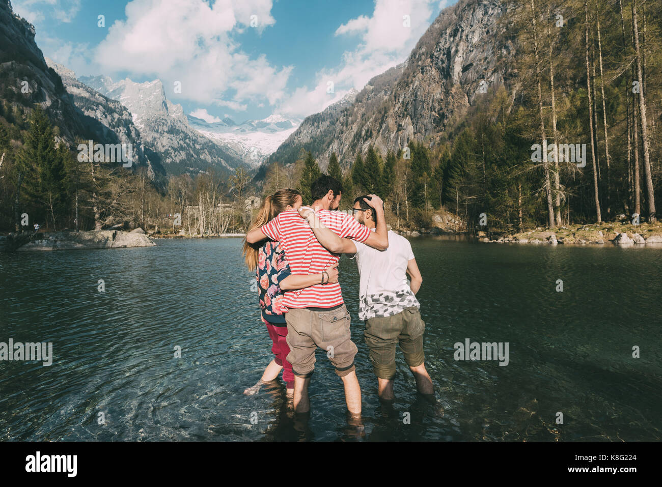 Vue arrière de trois jeunes amis adultes la cheville en lac de montagne, Lombardie, Italie Banque D'Images