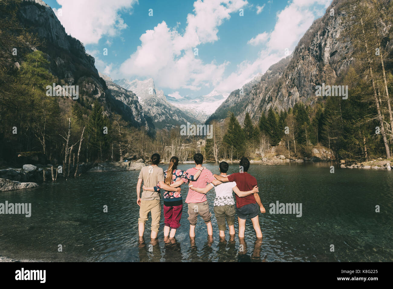Vue arrière de cinq amis adultes la cheville en lac de montagne, Lombardie, Italie Banque D'Images