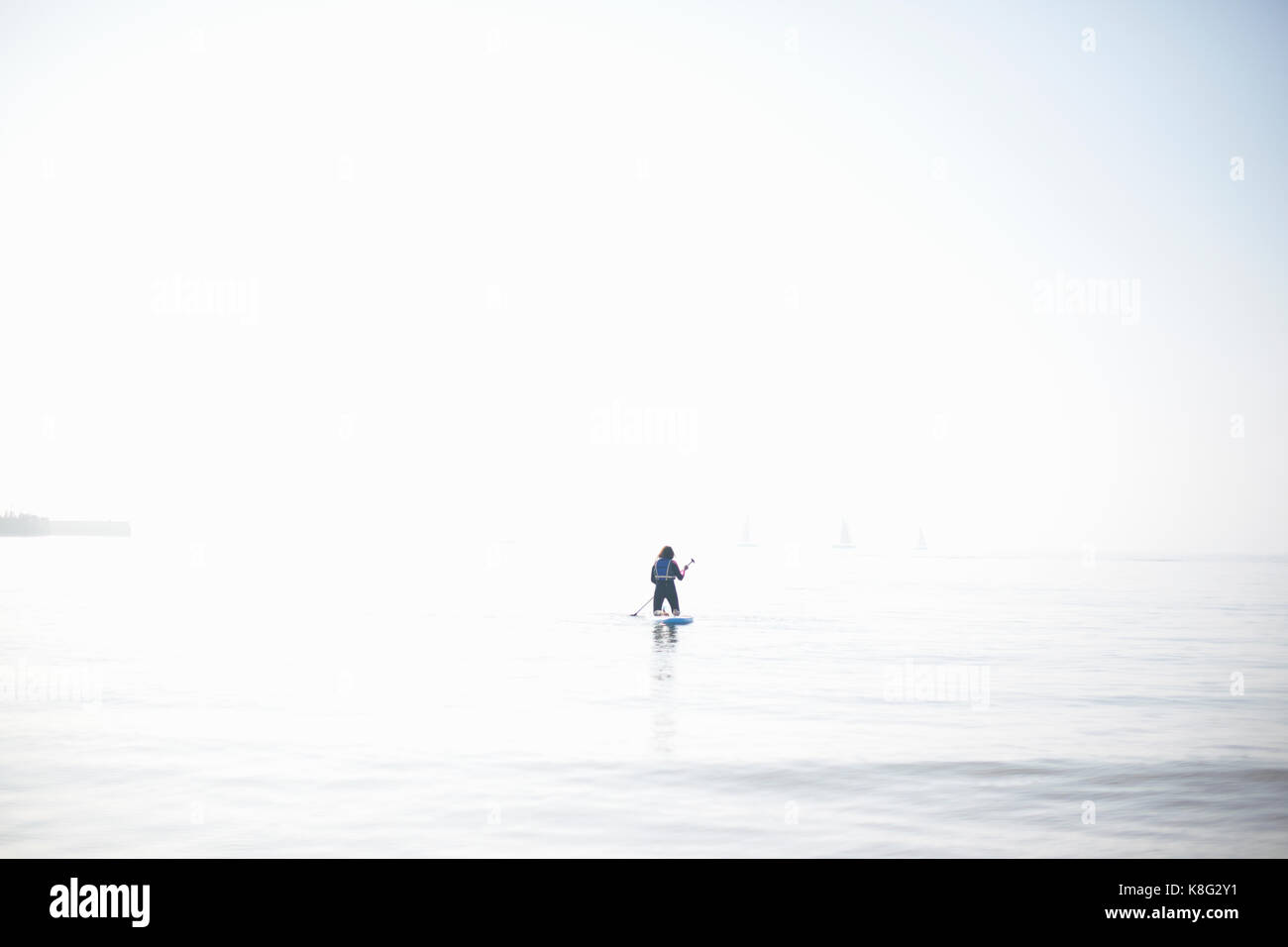 Vue éloignée sur femme paddleboarder paddling out sur la mer brumeuse Banque D'Images