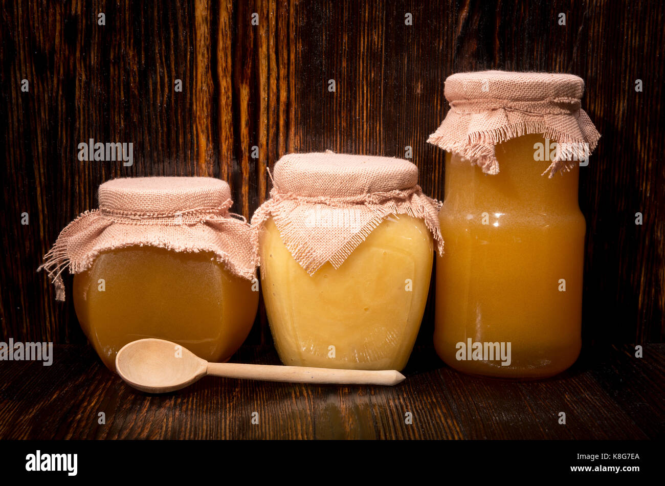 Trois pots de miel et une cuillère sur un fond de bois Banque D'Images