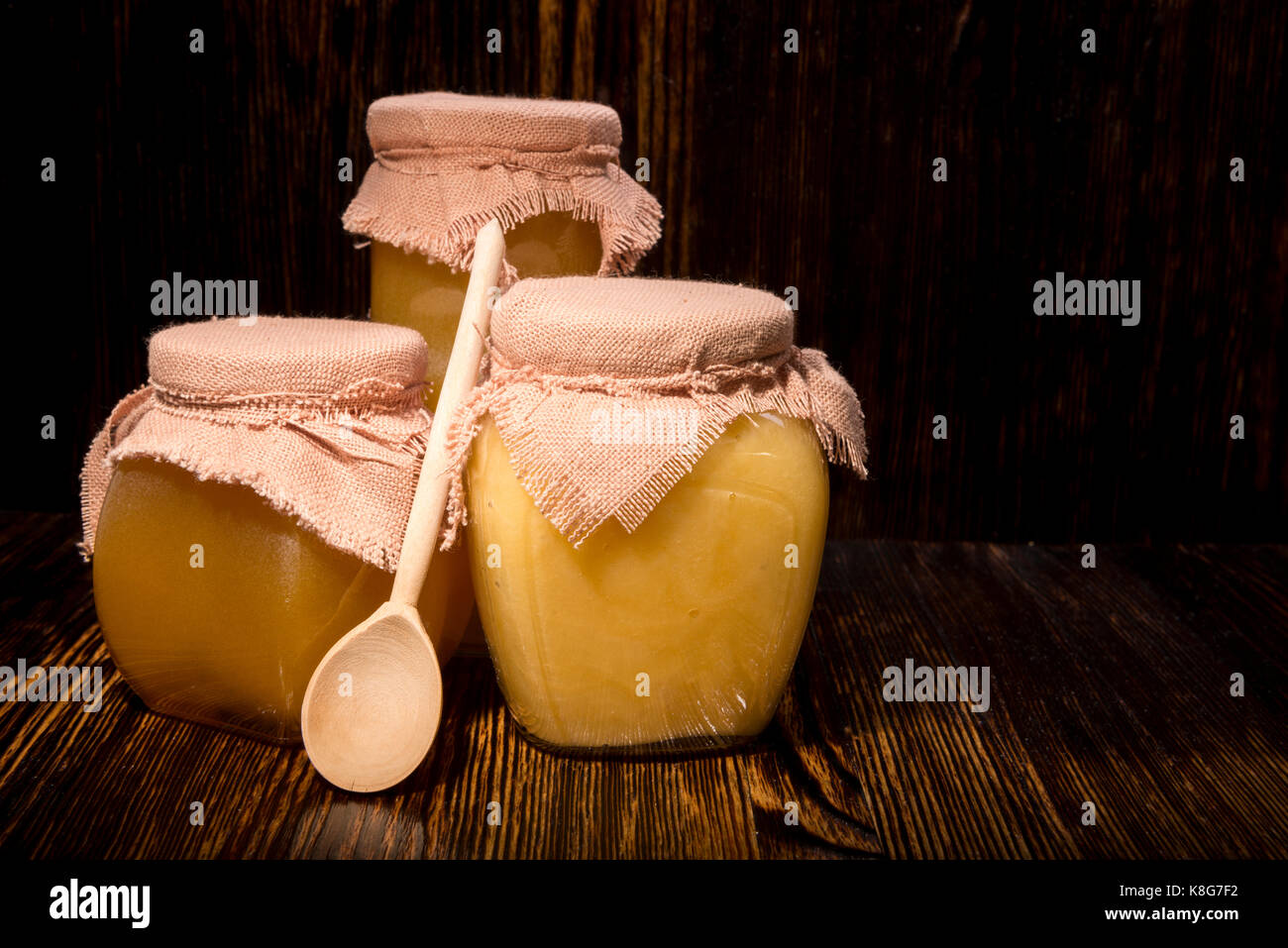 Trois pots de miel et une cuillère sur un fond de bois Banque D'Images