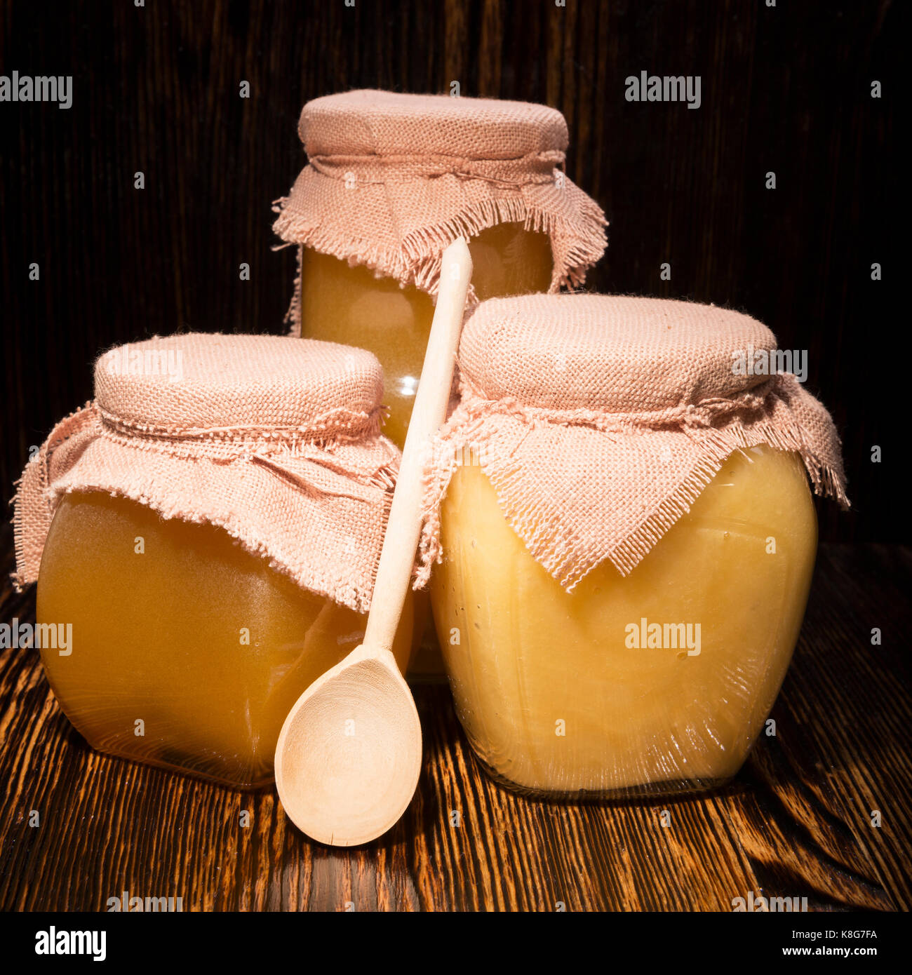 Trois pots de miel et une cuillère sur un fond de bois Banque D'Images