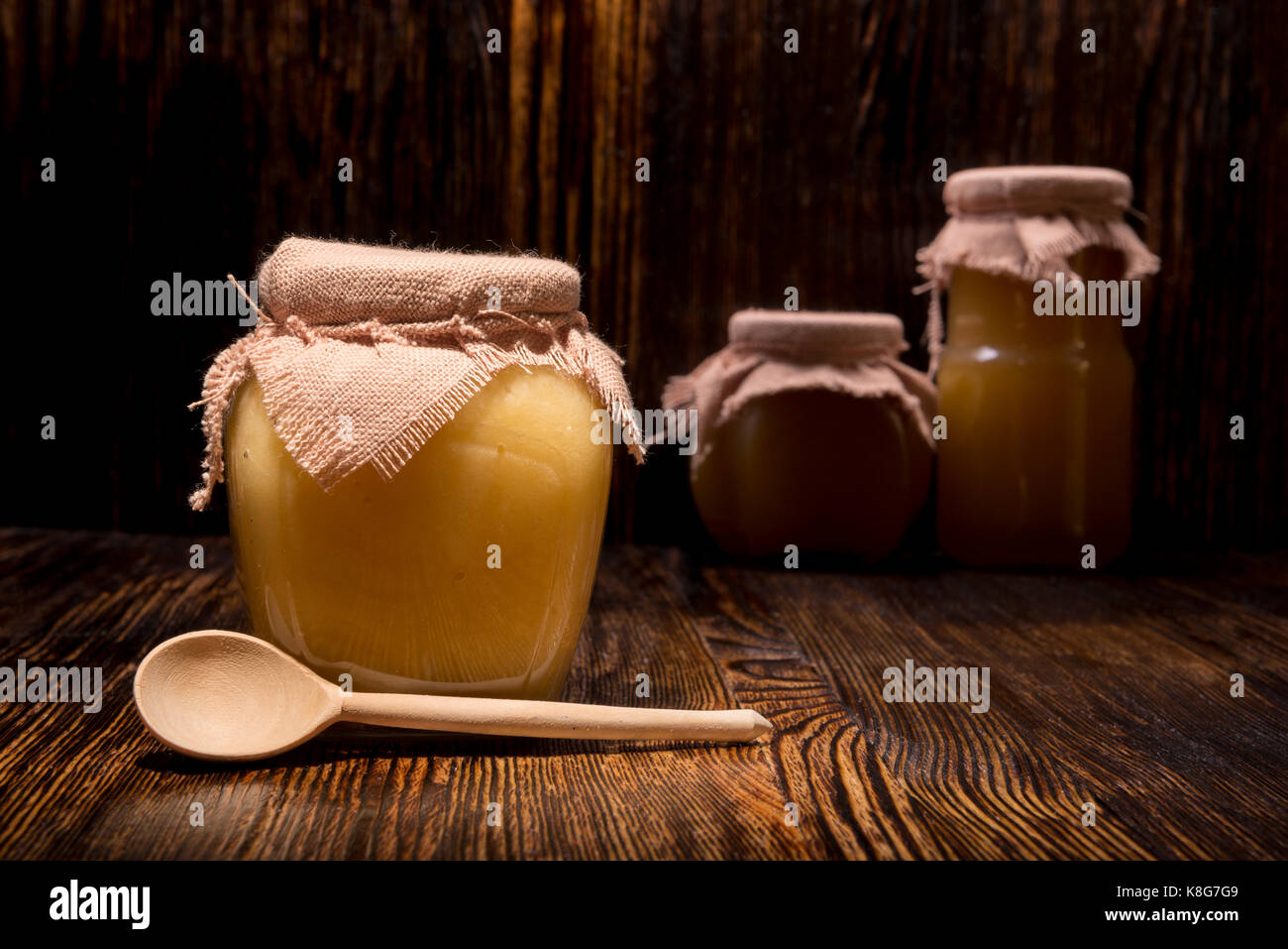 Trois pots de miel et une cuillère sur un fond de bois Banque D'Images