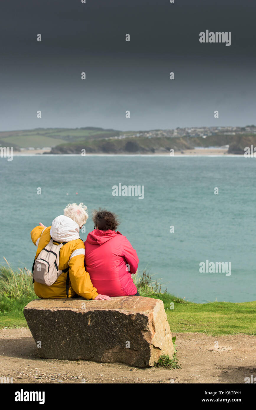 Newquay Cornwall - Deux promeneurs assis sur un rocher surplombant la baie de Newquay à peu dans fistral newquay, Cornwall Banque D'Images