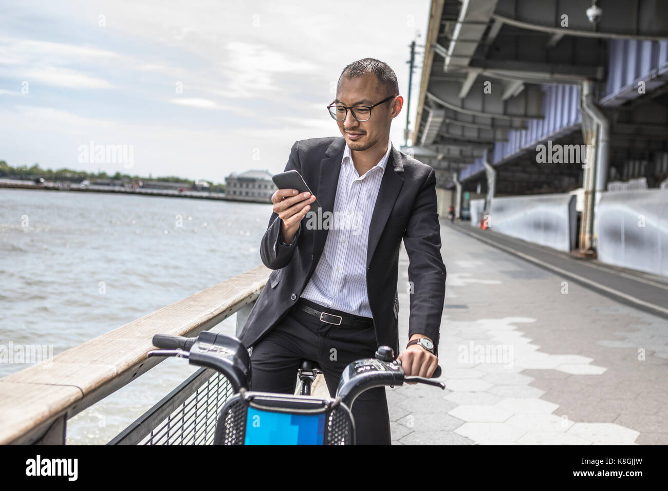 Cycliste businessman looking at smartphone sur front de mer, New York, USA Banque D'Images