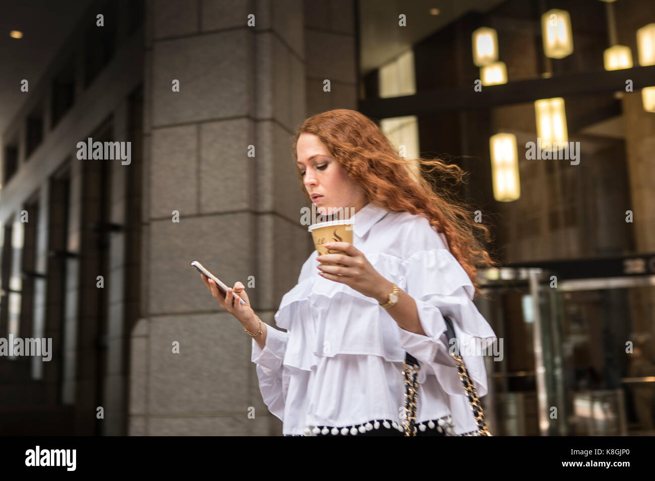 Café à emporter avec Young businesswoman looking at smartphone sur trottoir, New York, USA Banque D'Images