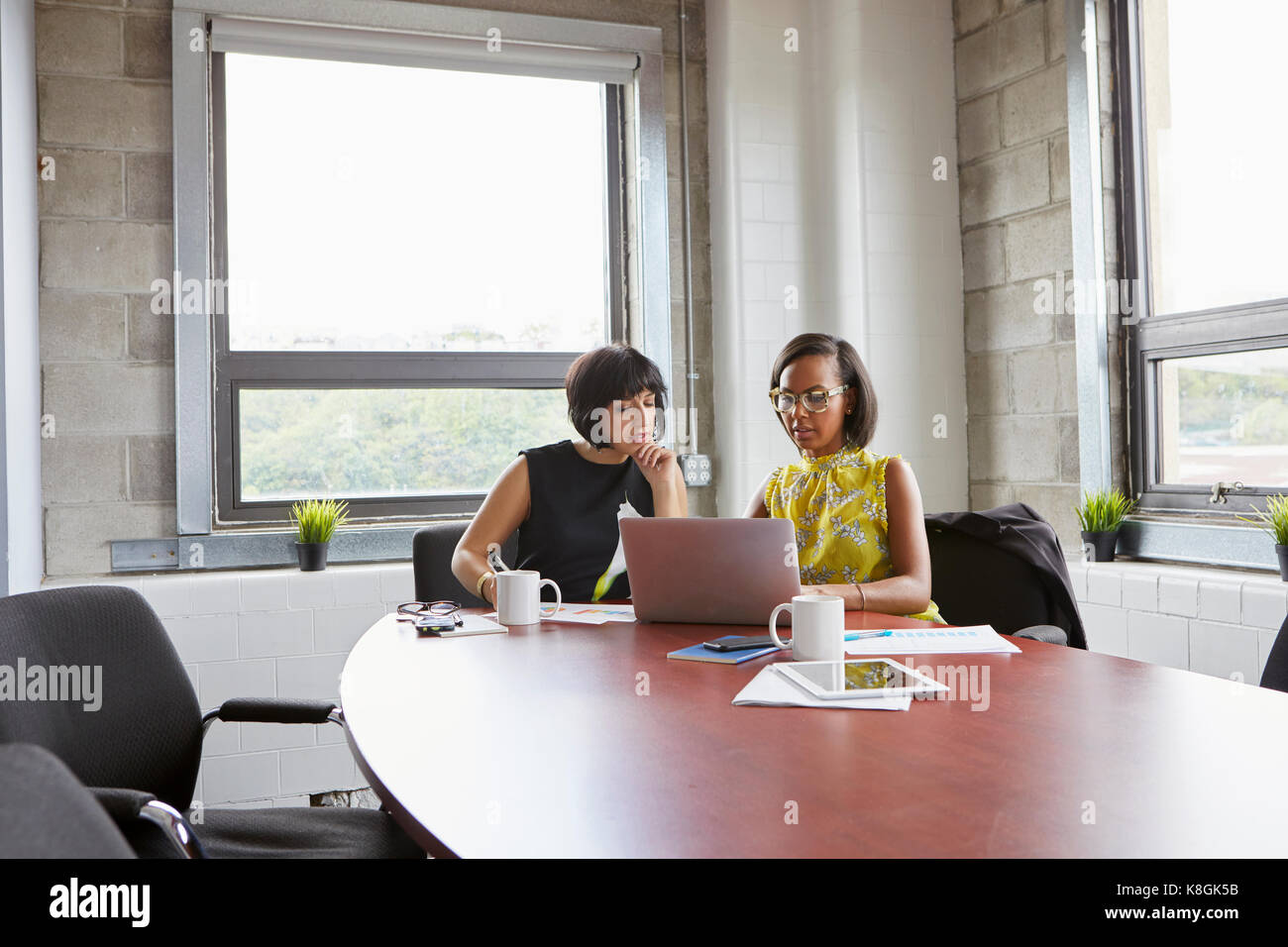 Deux femmes assises à la table de la salle de réunion, using laptop Banque D'Images