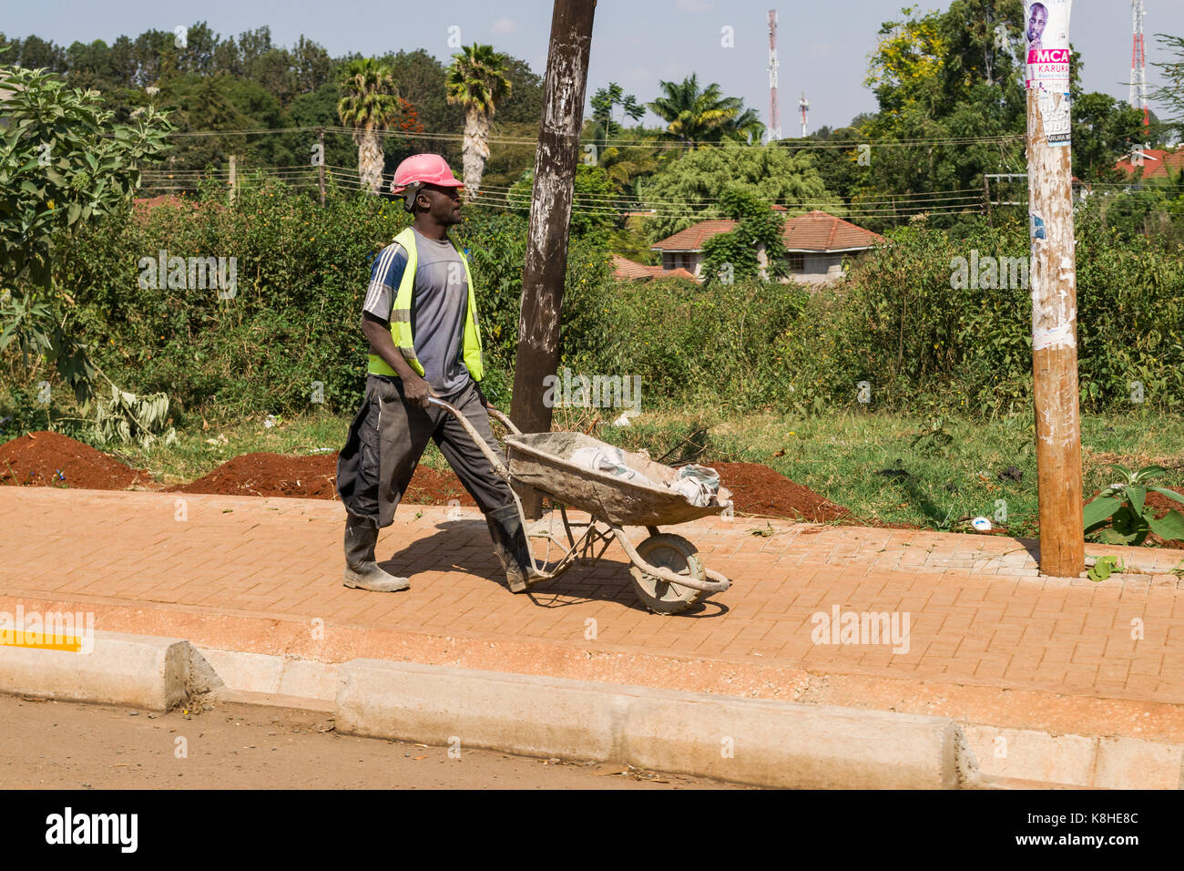 Construction Worker pushing wheelbarrow marche sur la chaussée, Nairobi, Kenya Banque D'Images