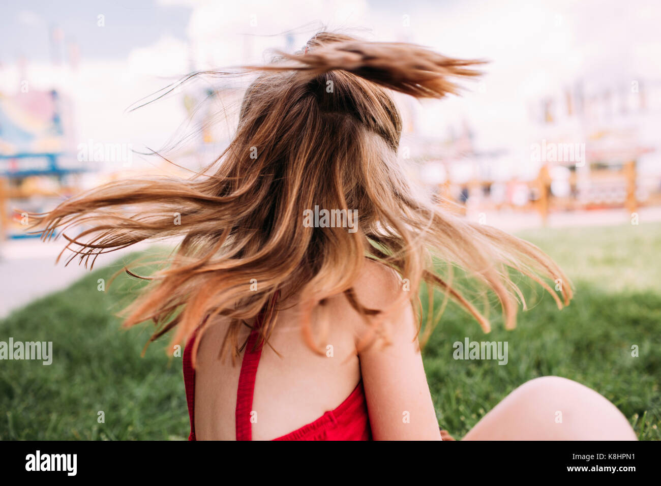 Playful girl tossing cheveux alors assis sur les champs du park Banque D'Images