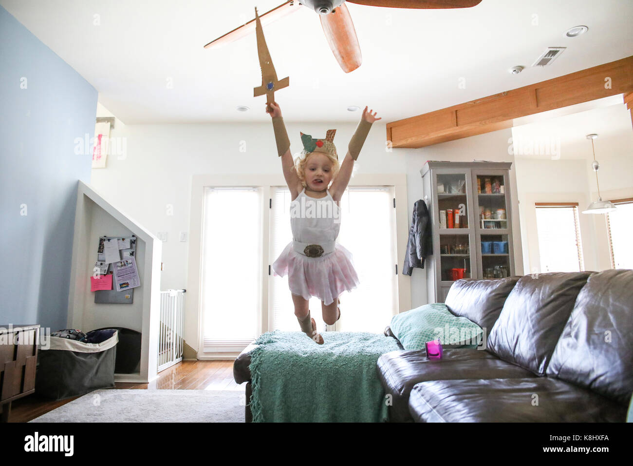 Fille avec couronne et l'épée d'un saut d'un canapé à la maison Banque D'Images