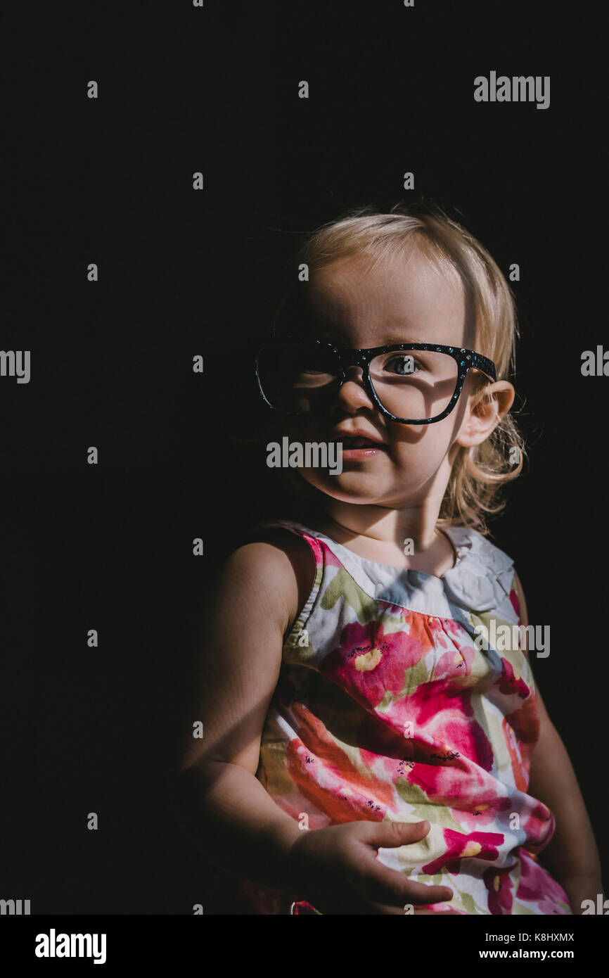 Portrait of cute baby girl wearing eyeglasses dans darkroom Banque D'Images
