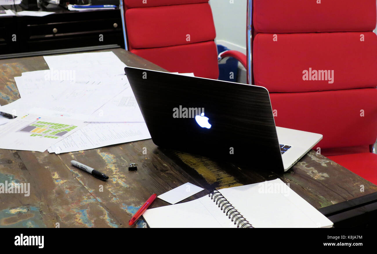 Deux chaises de bureau rouge assis à une table avec un livre de mac laptop sitting Ouvrir à côté d'une pile de papiers. Banque D'Images