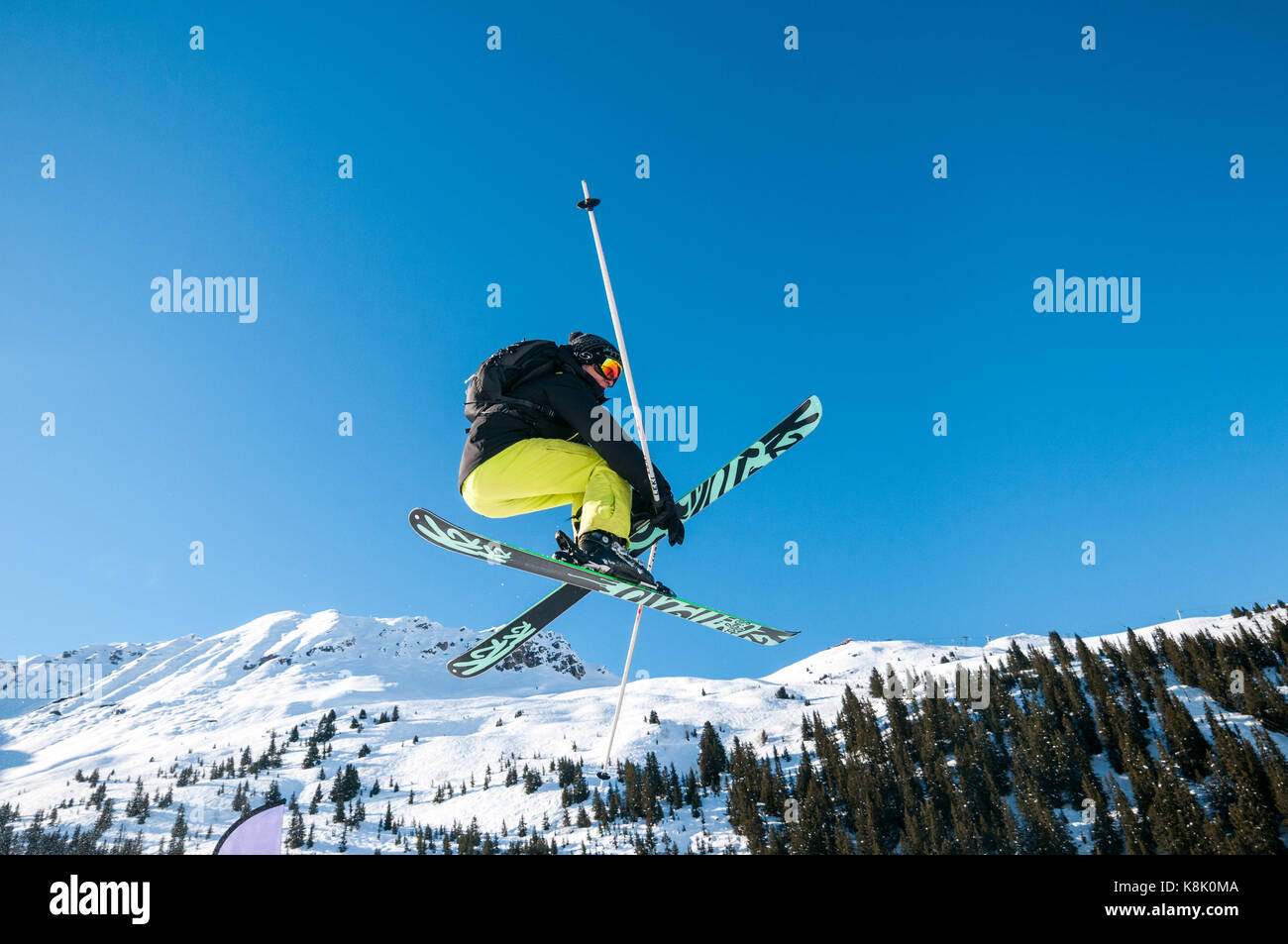 Male skier Jumping off ramp dans la neige à l'air sur un jour d'hiver ensoleillé avec des montagnes et arbres en arrière-plan, la station de ski des 3 Vallées, Meribel, France Banque D'Images