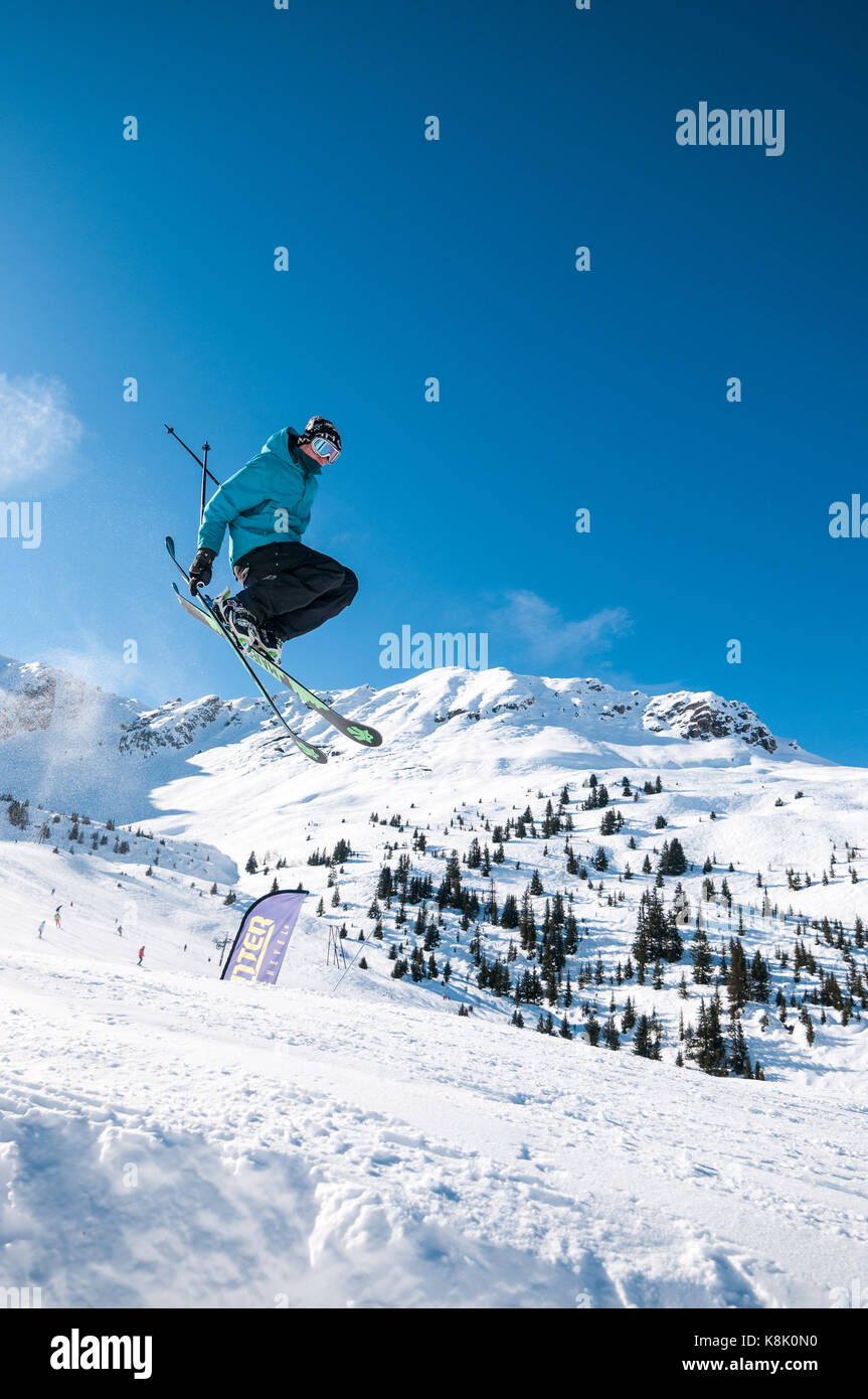 Male skier Jumping off ramp dans la neige à l'air sur un jour d'hiver ensoleillé avec des montagnes et arbres en arrière-plan, la station de ski des 3 Vallées, Meribel, France Banque D'Images