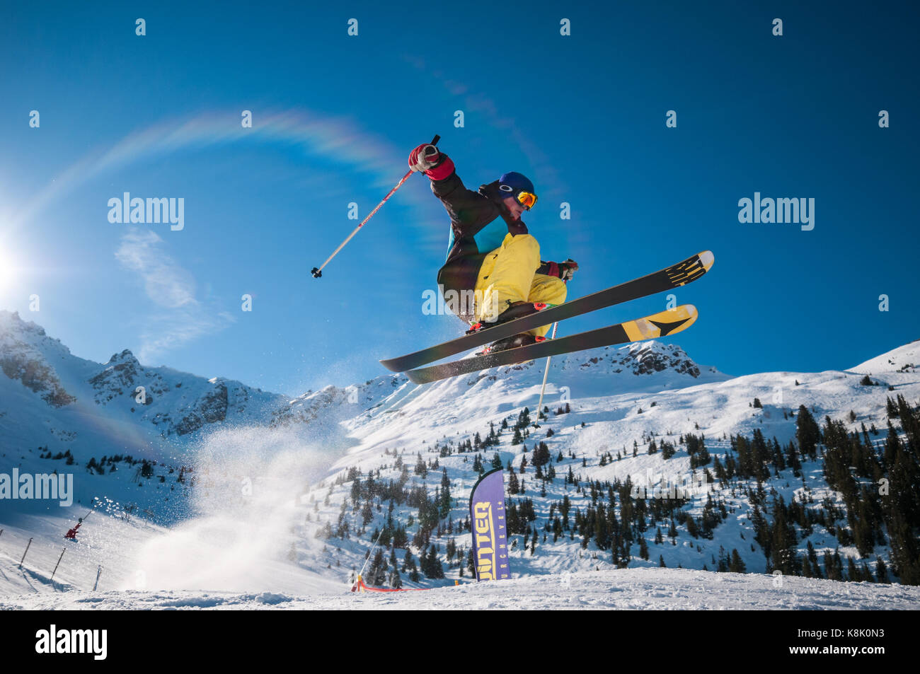 Male skier Jumping off ramp dans la neige à l'air sur un jour d'hiver ensoleillé avec des montagnes et arbres en arrière-plan, la station de ski des 3 Vallées, Meribel, France Banque D'Images
