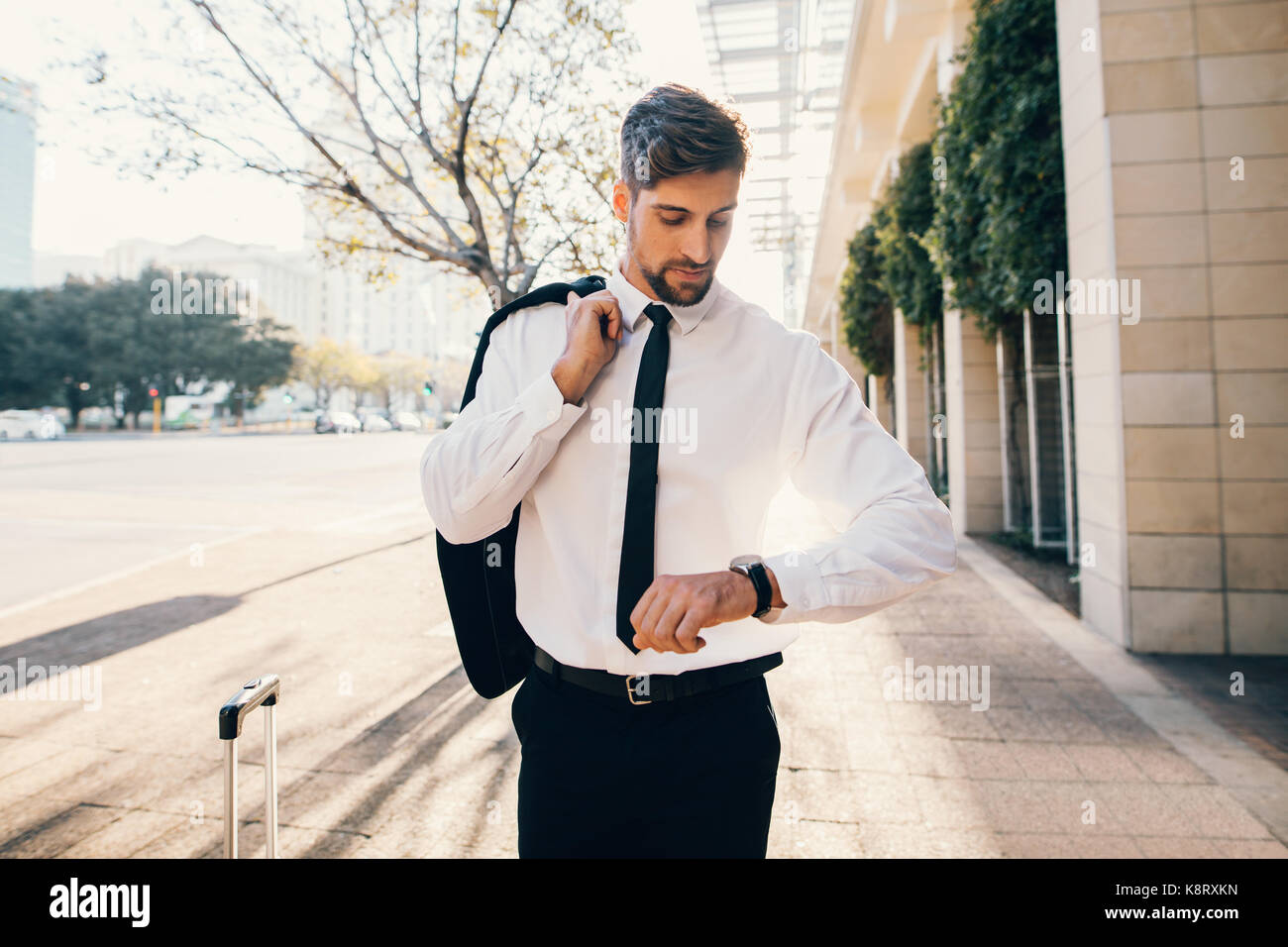 Beau jeune homme marchant à l'extérieur sur la rue et contrôler le temps. Caucasian businessman qui l'attendaient à l'aéroport et regardant sa montre. Banque D'Images