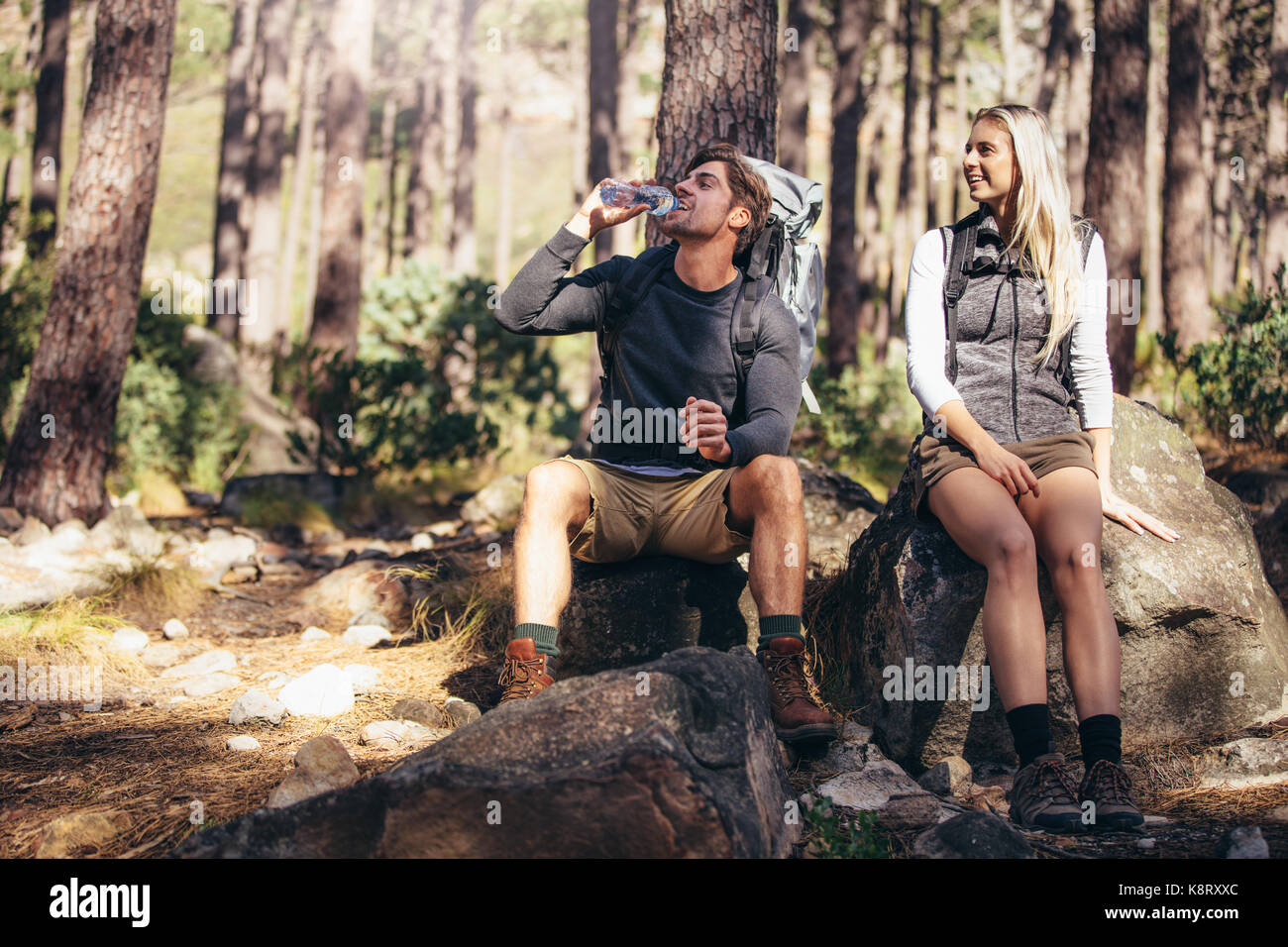 L'homme et la femme les randonneurs se détendre tout en trekking dans la forêt. Couple randonneur en faisant une pause assis sur le roc et l'eau potable. Banque D'Images