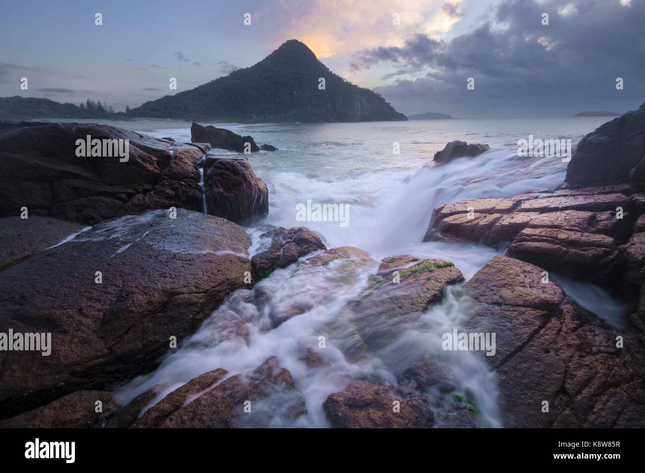 L'eau qui coule sur les rochers, plage au Zénith avec Mont Tomaree en arrière-plan, Port Stephens, NSW, Australie Banque D'Images