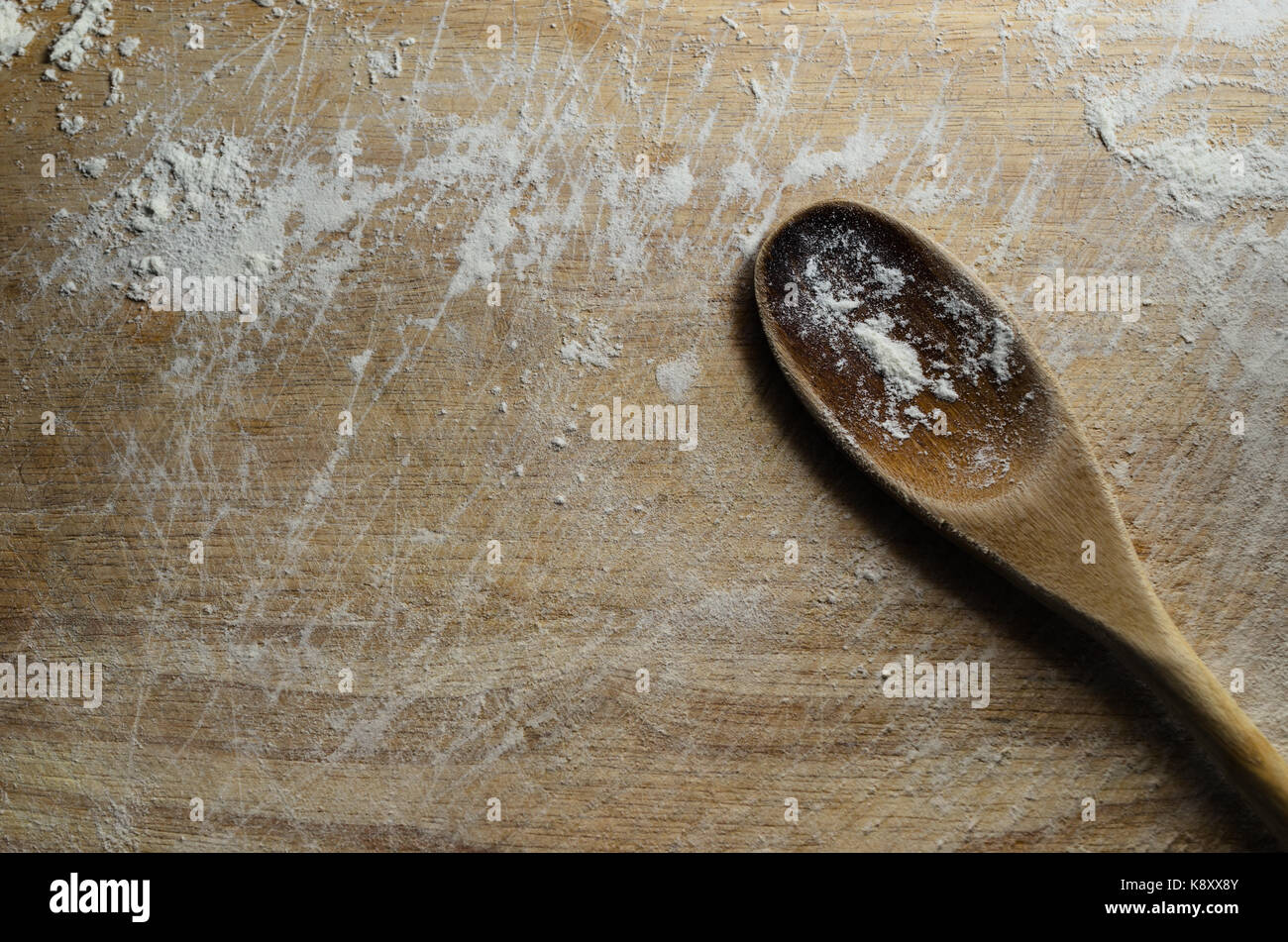 Passage tiré d'un employé et gratté ancienne en bois planche à découper avec la farine blanche. une cuillère en bois repose en diagonale sur sa surface. Banque D'Images